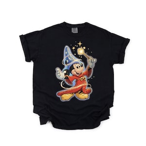 Peut inclure: T-shirt noir avec Mickey Mouse en dessin anim&eacute; v&ecirc;tu d'un costume de magicien. Mickey porte un chapeau de magicien bleu et une robe rouge, tenant une baguette lumineuse. Le motif comprend des &eacute;toiles et des &eacute;tincelles.