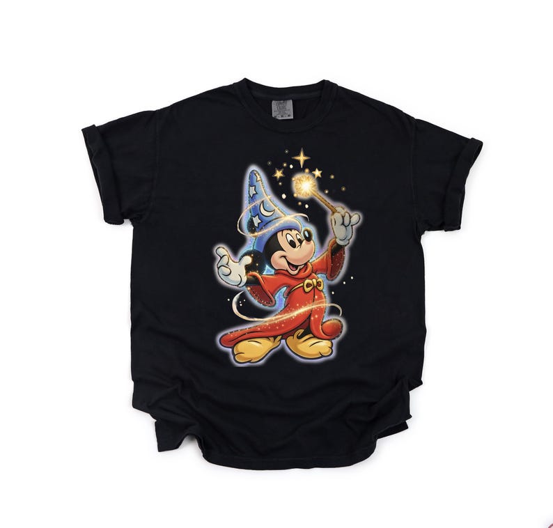 Peut inclure: T-shirt noir avec Mickey Mouse en dessin anim&eacute; v&ecirc;tu d'un costume de magicien. Mickey porte un chapeau de magicien bleu et une robe rouge, tenant une baguette lumineuse. Le motif comprend des &eacute;toiles et des &eacute;tincelles.