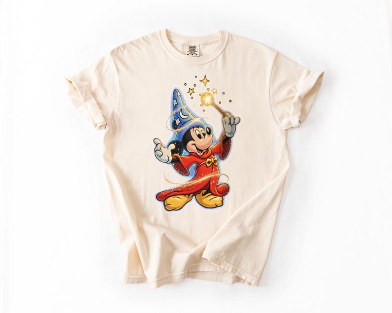 Peut inclure: T-shirt cr&egrave;me avec un dessin de Mickey Mouse en sorcier. Mickey porte un chapeau bleu &eacute;toil&eacute;, une robe rouge et tient une baguette magique dor&eacute;e. Le t-shirt a des manches retrouss&eacute;es.