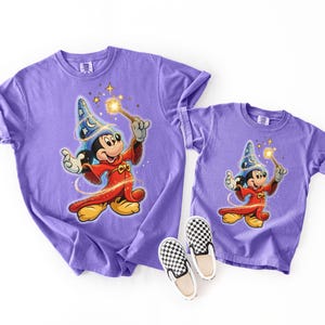 Peut inclure: Deux t-shirts violets, une taille adulte et une taille enfant, avec un dessin de Mickey Mouse en magicien avec une baguette. Les t-shirts sont assortis de chaussures &agrave; enfiler &agrave; carreaux noirs et blancs. Les t-shirts sont en mati&egrave;re souple.