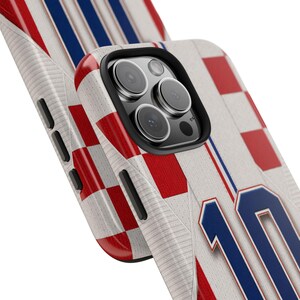 May include: A phone case featuring a design inspired by a sports jersey. The case has a white background with red and blue accents, including a checkered pattern and the number 10 in blue. The case is designed to fit a smartphone.