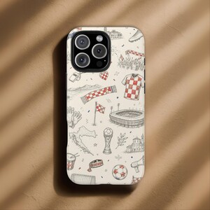 May include: A phone case with a cream background featuring a hand-drawn design of Croatian soccer-themed elements. The design includes a soccer ball, a checkered jersey, a stadium, a trophy, and a map of Croatia.