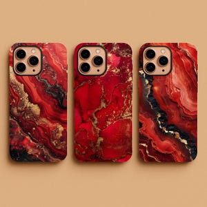 May include: Three phone cases with a vibrant red, black, and gold marble design. The cases have a glossy finish and are designed to fit a smartphone. The marble pattern features flowing lines and swirls, creating a unique look.