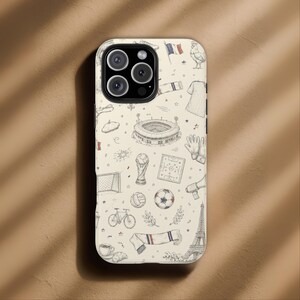 May include: A phone case with a cream background and a repeating pattern of French-themed illustrations in black and white. The design includes a soccer ball, Eiffel Tower, and a beret.