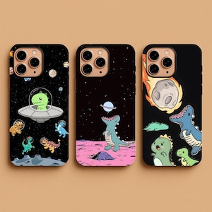 May include: Three black phone cases with colorful dinosaur designs. One case features a green dinosaur in a spaceship, another shows a dinosaur with a planet, and the third has dinosaurs with a meteor.