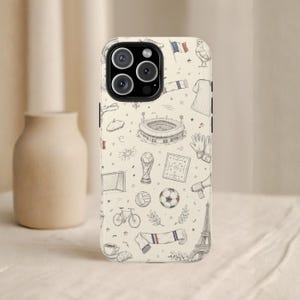 May include: A phone case with a cream background featuring a repeating pattern of French-themed illustrations. The drawings include a soccer ball, a stadium, a trophy, a bicycle, a croissant, and the Eiffel Tower.