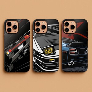 May include: Three black phone cases with car illustrations. The cases feature stylized graphics of classic cars in black, white, red, and blue. The designs showcase different angles of the vehicles, including front, side, and rear views.