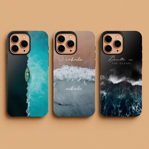 May include: Three phone cases with ocean-themed designs. One case features a boat on turquoise water, another has a beach scene with the words "inhale exhale", and the third displays ocean waves with the text "Breathe in the ocean".