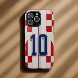 May include: A phone case featuring a design inspired by a sports jersey. The case has a white background with red and blue checkered patterns and vertical stripes. The number "10" is prominently displayed in blue.