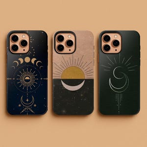 Op de afbeelding: Drie telefoonhoesjes met hemelse ontwerpen. Eén hoesje is donkerblauw met een gouden zon en maanfasen. Een andere heeft een zon en maan over een zwart-beige achtergrond. De derde is donkergroen met een maansikkelontwerp.