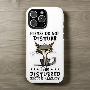 May include: White phone case with a cartoon cat illustration. The cat has a grumpy expression and is surrounded by the text "PLEASE DO NOT DISTURB" and "I AM DISTURBED ENOUGH ALREADY".