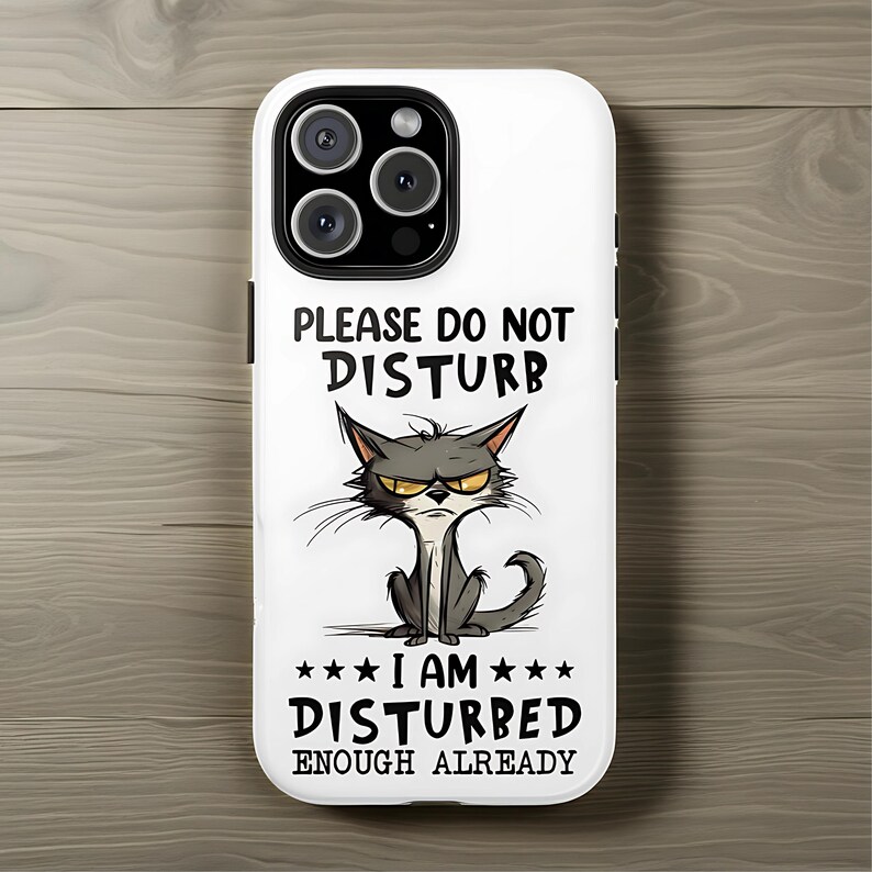 May include: White phone case with a cartoon cat illustration. The cat has a grumpy expression and is surrounded by the text "PLEASE DO NOT DISTURB" and "I AM DISTURBED ENOUGH ALREADY".
