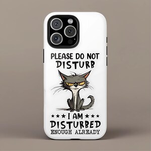 May include: White phone case with a cartoon cat illustration. The cat has an angry expression and is gray with yellow eyes. Text on the case reads "PLEASE DO NOT DISTURB" and "I AM DISTURBED ENOUGH ALREADY."