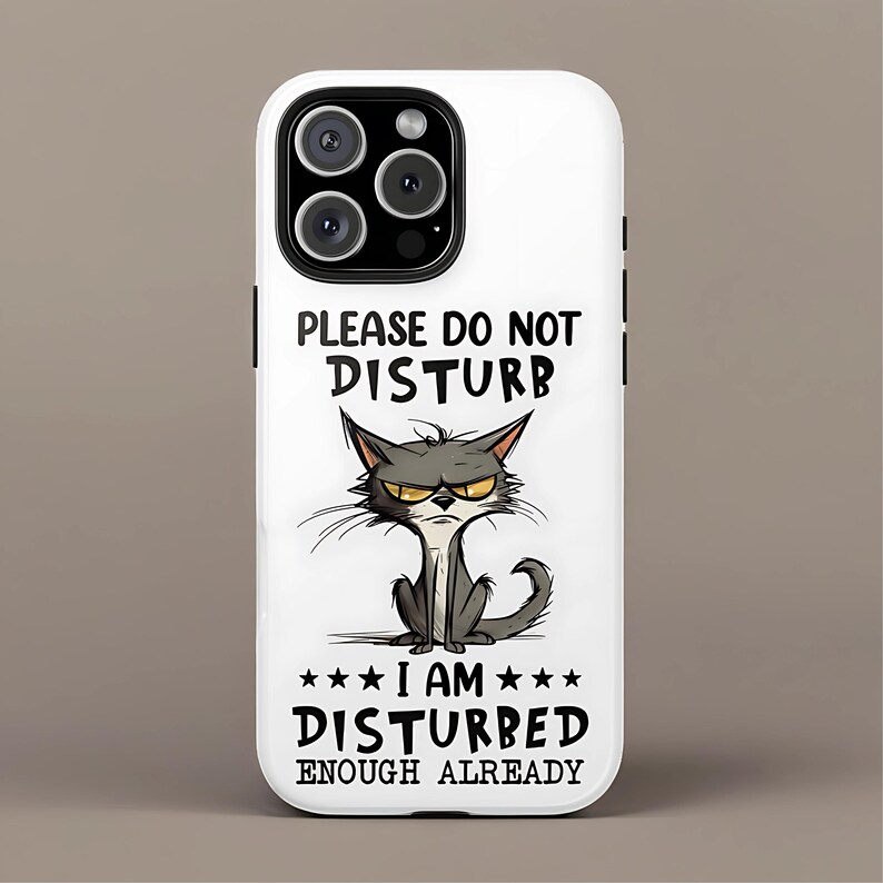 May include: White phone case with a cartoon cat illustration. The cat has an angry expression and is gray with yellow eyes. Text on the case reads "PLEASE DO NOT DISTURB" and "I AM DISTURBED ENOUGH ALREADY."