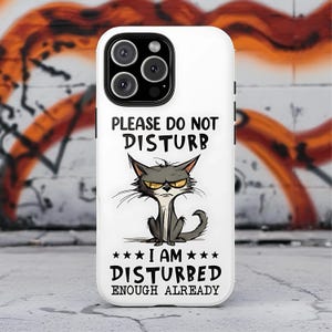 May include: White phone case with a cartoon image of a grumpy gray cat. The text on the case reads "PLEASE DO NOT DISTURB" above the cat and "I AM DISTURBED ENOUGH ALREADY" below it. The case has a black camera lens.