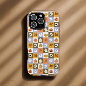 Op de afbeelding: Een telefoonhoesje met een herhalend Halloween-patroon. Het ontwerp bevat pompoenen, geesten, schedels, bloemen en herfstbladeren in een rasterpatroon. De hoes heeft een transparante rand en een uitsparing voor een camera met meerdere lenzen.