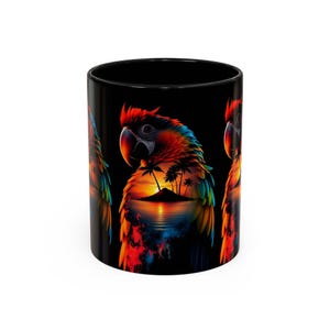 Puede incluir: Una taza de cerámica negra con una ilustración de un loro de colores vibrantes. El plumaje del loro incorpora una escena de atardecer tropical con palmeras, una pequeña isla y una superficie oceánica reflectante en tonos naranja, amarillo y azul.