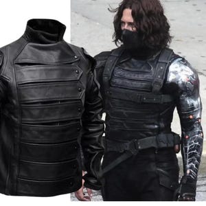 May include: Black leather jacket with a high collar and multiple horizontal bands across the chest. The jacket has a military-inspired design with button details. The image also shows a black tactical vest and a metal arm.