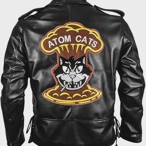 May include: Black leather jacket with a large embroidered patch on the back. The patch features a cartoon cat smoking a cigarette, with the words "ATOM CATS" above it in yellow lettering. The jacket has a classic biker style with a notched collar and zippered pockets.