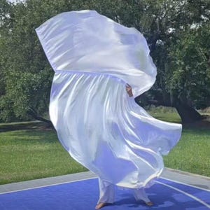 May include: A large, flowing white worship flag made of lightweight, semi-sheer fabric. The material is gathered at the top, creating a wide, expansive arc that catches the air, displaying a smooth, satin-like sheen across the entire surface.