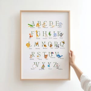 May include: A framed alphabet print featuring colorful animal illustrations for each letter. The print includes animals like an alligator, bear, fox, giraffe, lion, monkey, owl, panda, rabbit, sheep, tiger, whale, and zebra. The print is in a light wooden frame.