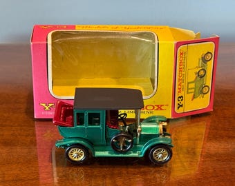 May include: A green Matchbox Y-3 1906 Benz Limousine toy car with a black roof and gold-colored wheels. The toy car is in front of its original pink and yellow box.