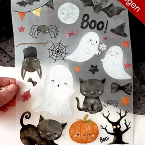Könnte beinhalten: Ein transparenter Bogen mit Halloween-Aufklebern im Aquarellstil, darunter Geister, schwarze Katzen, Fledermäuse, ein Kürbis, eine Spinne, ein Netz und Wimpel. Der Text "Boo!" erscheint zweimal, und der Bogen ist mit "Dina4 XL Bogen" sowie der Website "www.herzchendinge.de" unten beschriftet.
