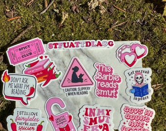May include: A collection of colorful stickers with various designs and text. The stickers feature phrases like "Spicy Book Club," "This Barbie reads smut," and "Boys in books are better." Other designs include chili peppers, hearts, and a skull reading a book.
