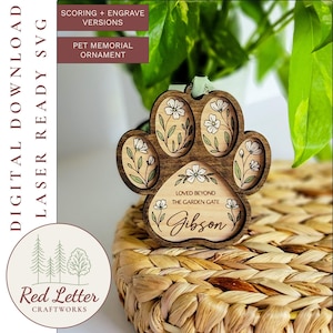 Könnte beinhalten: Ein hölzernes Gedenk-Ornament für Haustiere in Form eines Pfotenabdrucks mit floralen Designs und dem Namen "Gibson". Das Ornament enthält den Text "Loved Beyond The Garden Gate". Der Hintergrund umfasst einen geflochtenen Korb und Grün.