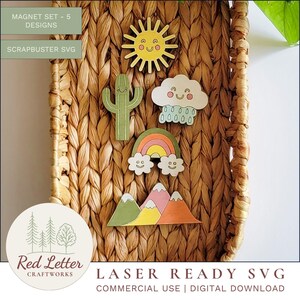 May include: A collection of five wooden magnets with a playful design. The magnets feature a smiling sun, a cactus, a cloud with raindrops, a rainbow, and a mountain range. They are presented against a woven background.