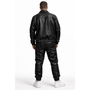 Puede incluir: Conjunto de chaqueta y pantal&oacute;n de cuero negro. La chaqueta tiene cuello y dobladillo de canal&eacute;. El pantal&oacute;n tiene cintura y pu&ntilde;os el&aacute;sticos. El conjunto se lleva con zapatillas blancas.