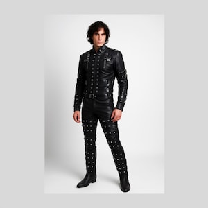 Puede incluir: Conjunto de chaqueta y pantalón de cuero negro. La chaqueta presenta un cuello alto, múltiples botones y detalles metálicos decorativos. Los pantalones son ajustados y adornados con tachuelas metálicas. El conjunto se completa con botas negras.