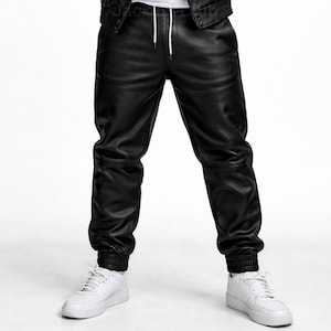Puede incluir: Pantalones deportivos de cuero negro con cintura con cord&oacute;n y pu&ntilde;os el&aacute;sticos. Los pantalones se combinan con zapatillas blancas. Los pantalones de cuero tienen un corte relajado.