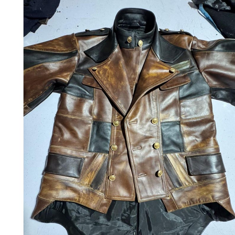 May include: A brown and black leather jacket with a patchwork design. The jacket features a double-breasted front with gold-colored buttons, a black collar, and black accents. The jacket has a vintage, distressed look.