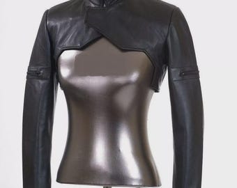 May include: A black leather cropped jacket with a high collar and long sleeves. The jacket has a unique design with a cut-out in the front and a zipper closure.