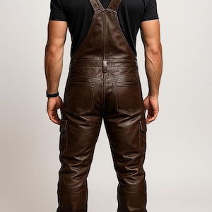 May include: Brown leather overalls with cargo pockets and suspender straps. The overalls are worn with a black t-shirt and brown boots. The image is taken from the back, showcasing the details of the leather and the overall design.