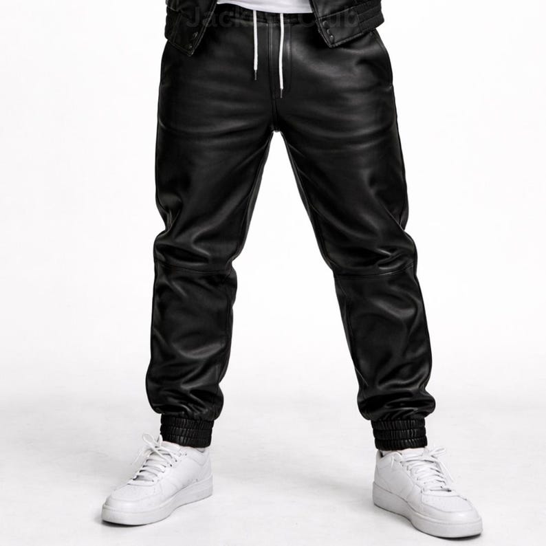 Puede incluir: Pantalones deportivos de cuero negro con cintura con cord&oacute;n y pu&ntilde;os el&aacute;sticos. Los pantalones se combinan con zapatillas blancas. Los pantalones de cuero tienen un corte relajado.