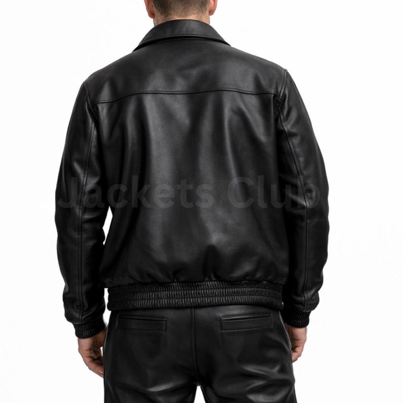 Puede incluir: Chaqueta de cuero negra con cuello, cintura y pu&ntilde;os el&aacute;sticos. La parte trasera de la chaqueta es visible, con el texto "Jackets Club" impreso en la parte inferior izquierda. La chaqueta es parte de un conjunto de ropa de cuero.