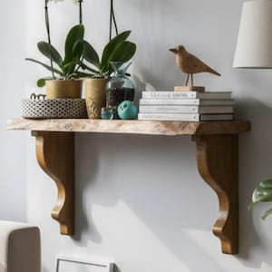 Op de afbeelding: Een woonkamer met een houten plank met potorchideeën, boeken en een houten vogelbeeldje. Daaronder zijn ingelijste foto's en een bank met kussens te zien. Een staande lamp en een potplant maken de decoratie compleet.