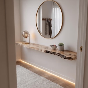 May include: A modern entryway featuring a floating wooden shelf with a live edge, a round gold mirror, and a small table lamp. A small succulent in a gray pot and a decorative bowl sit on the shelf. The room has a white wall and a white rug.