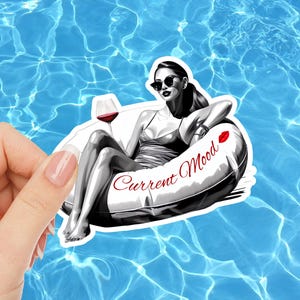 May include: A sticker featuring a grayscale illustration of a person relaxing in a pool float with a glass of wine. The text "Current Mood" is written on the float. The background is a blue pool.