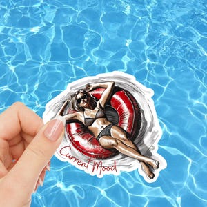 May include: A sticker featuring an illustration of a person in a bikini relaxing on a red and white inflatable ring. The sticker has the text "Current Mood" and the signature "jBelly". The background is a blue water pattern.