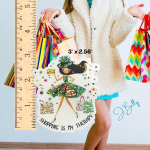 May include: A decorative sticker featuring a fashion illustration of a woman in a green dress and hat, holding a gold clutch and shopping bags. The sticker is approximately 3 inches by 2.56 inches and has the text "SHOPPING IS MY THERAPY".