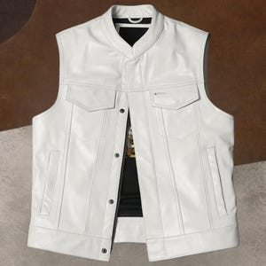 Puede incluir: Un chaleco de cuero blanco con cuello mandarín y dos bolsillos en el pecho. El chaleco tiene una botonadura frontal y dos bolsillos laterales. El chaleco es sin mangas y parece estar hecho de cuero liso y de alta calidad.