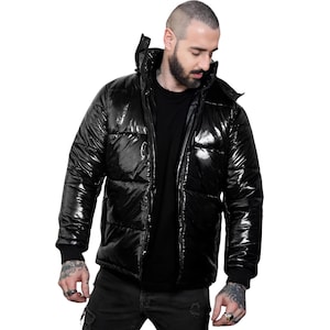 May include: A shiny black puffer jacket with a high collar and a zip-up front. The jacket has a glossy finish and a quilted design. The sleeves have black ribbed cuffs. The jacket is worn over a black shirt.