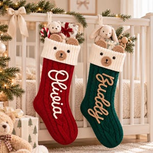 May include: Two knitted Christmas stockings, one red and one dark green, featuring white ribbed cuffs with bear faces. The red stocking has the name Olivia in white script, and the green stocking has the name Buddy in tan script, both filled with toys.