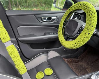 Peut inclure: Accessoires de voiture au crochet vert citron, dont un couvre-volant, des housses de ceinture de sécurité et deux dessous de verre. Les articles sont placés à l'intérieur d'une voiture avec des sièges en cuir noir.