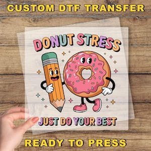 May include: A DTF transfer featuring a cartoon donut and pencil with the text "DONUT STRESS JUST DO YOUR BEST". The donut has pink frosting and the pencil is orange. The transfer is ready to press.