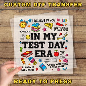 May include: A DTF transfer sheet with the text "CUSTOM DTF TRANSFER" at the top and "READY TO PRESS" at the bottom. The design features colorful school-themed graphics and the phrase "IN MY TEST DAY ERA".