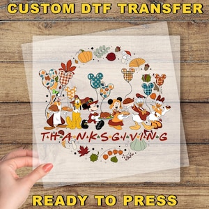 May include: A custom DTF transfer sheet featuring a Thanksgiving-themed graphic with cartoon characters, including Mickey and friends, surrounded by autumn leaves, pumpkins, and acorns. The text "THANKSGIVING" is printed in a bold, brown font.